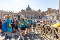 Gruppe von Pilgern mit türkisfarbenen T-Shirts und Strohhüten auf dem Petersplatz vor dem Petersdom bei sonnigem Wetter